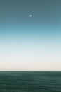 Vertical shot of a beautiful view of ocean under the moon in the blue sky Royalty Free Stock Photo