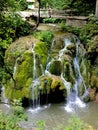 Vertical shot of a beautiful waterfall over the moss-covered rocks under the wooden bridge Royalty Free Stock Photo