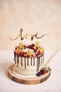 Vertical shot of a beautiful wedding cake with fruits chocolate drip and with Love topper