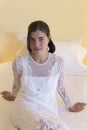 Brunette girl wearing long white lace dress sitting on bed