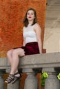 Beautiful young woman in cropped white top and short red skirt sitting on stone balustrade