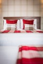 Vertical shot of a bed with red and brown square pattern pillows and white sheets Royalty Free Stock Photo