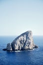 Vertical shot of a big rock in the middle of the sea with a blue sky in the background Royalty Free Stock Photo