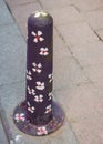 Vertical shot of a black colored metallic object with pictures of white flowers on the street