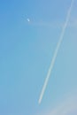 Vertical shot of the blue beautiful sky with airplane engine trails and the half-moon Royalty Free Stock Photo