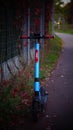 Vertical shot of a blue electric rental Spot brand scooter on a footpath by a grid fence