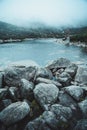 Vertical shot of a blue river flowing in a forest with a pile of rocks in the foreground Royalty Free Stock Photo