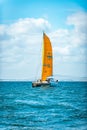 Vertical shot of a boat with an orange sail cruising under a cloudy blue sky