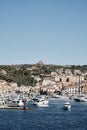 Vertical shot of boats on the water near buildings on the hill with a blue sky in the background