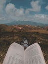 Vertical shot of a book and feet of a person on the hill in gloomy day