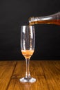 Vertical shot of a bottle of champagne being poured into a glass on a wooden table