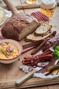 Vertical shot of a bowl of hummus on a wooden cutting board with bread and sausages on a table