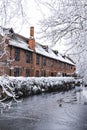 Vertical shot of a brick building next to a river in winter covered in white snow in London