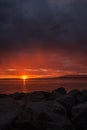 Vertical shot of a bright orange red sunset sky over a rocky seashore Royalty Free Stock Photo