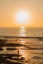 Vertical shot of a bright sun setting on the orange horizon and a man standing on the beach Royalty Free Stock Photo