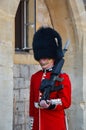 Vertical shot of a british guard carrying a weapon, with a red uniform and a black fur hat.