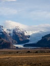 Vertical shot of a brown soil field with rocky mountains and glacier fading in from the sky, Iceland Royalty Free Stock Photo