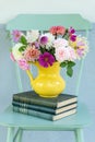 Vertical shot of a bunch of assorted colorful flowers in a vase on top of stacked books on a chair