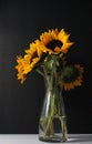 Vertical shot of a bunch of sunflowers in a glass vase on the table in the dark background Royalty Free Stock Photo