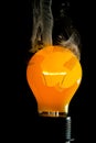 Vertical shot of a burning light bulb with smoke coming out of it isolated on a black background Royalty Free Stock Photo