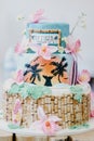 Vertical shot of a cake with Hawaiian decorations with pink flowers, palms and the word ALOHA