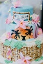 Vertical shot of a cake with Hawaiian decorations with pink flowers, palms and the word ALOHA