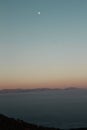 Vertical shot of a calm sea with the moon visible in the sky