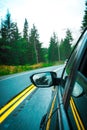 Vertical shot of a car driving on a paved road bend with a forest and the sky in the background.