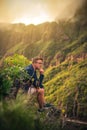 Vertical shot of a caucasian male sitting on the edge of a green cliff and thinking at sunset Royalty Free Stock Photo