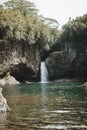 Vertical shot of a channel coming through a cave in the wilderness into a green pond Royalty Free Stock Photo