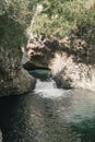 Vertical shot of a channel coming through a cave in the wilderness into a green pond Royalty Free Stock Photo