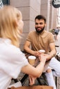 Vertical shot of cheerful young dating couple having coffee together sitting at table holding hands in street cafe on Royalty Free Stock Photo