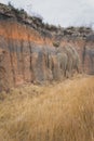 Vertical shot of a clay cliff that falls into dry brown grass Royalty Free Stock Photo