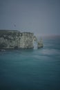 Vertical shot of coastal cliffs against sea waves on a cloudy day Royalty Free Stock Photo