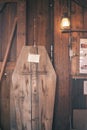 Vertical shot of a coffin made with plywood with a cross carving and a light bulb hanging on a door