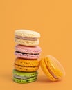Vertical shot of colorful balancing macaroons against a yellow background