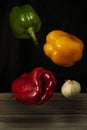 Vertical shot of colorful bell peppers and a bulb of garlic in the air above a wooden surface