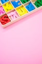 Vertical shot of colorful wooden letters in their case, placed on a pink surface Royalty Free Stock Photo