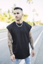 Vertical shot of a cool young man with tattoos wearing a black t-shirt standing on the street Royalty Free Stock Photo