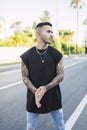 Vertical shot of a cool young man with tattoos wearing a black t-shirt standing on the street Royalty Free Stock Photo