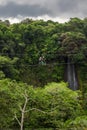 vertical shot couple of hikers with harness and helmet riding zipline bicycles surrounded by vegetation and a beautiful waterfall