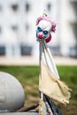 Vertical shot of the creepy mask of a clown on a rusty rod with a worn flag in the park