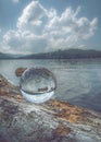 Vertical shot of a crystal ball on a fallen tree log, reflecting a tranquil lake on a cloudy day Royalty Free Stock Photo