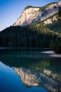 Vertical shot of a crystal clear lake near base of a white mountain with green pine tree forest Royalty Free Stock Photo