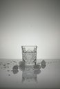 Vertical shot of crystal water glass, ice cubes and waterdrops around, on a white shiny surface Royalty Free Stock Photo