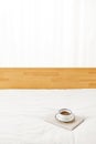 Vertical shot of a cup of coffee on a journal on white bedsheets under the lights