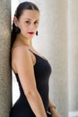 Vertical shot of a curly-haired brunette young woman leaning against a gray stone column Royalty Free Stock Photo