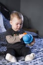 Vertical shot of cute fair baby girl sitting on bed examining duck toy Royalty Free Stock Photo