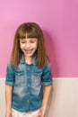 Vertical shot of a cute girl with crimped hair and bangs posing in front of a pink wall Royalty Free Stock Photo