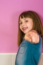 Vertical shot of a cute girl with crimped hair and bangs posing in front of a pink wall Royalty Free Stock Photo